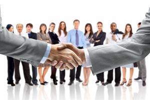 business handshake with team of co-workers in the background 